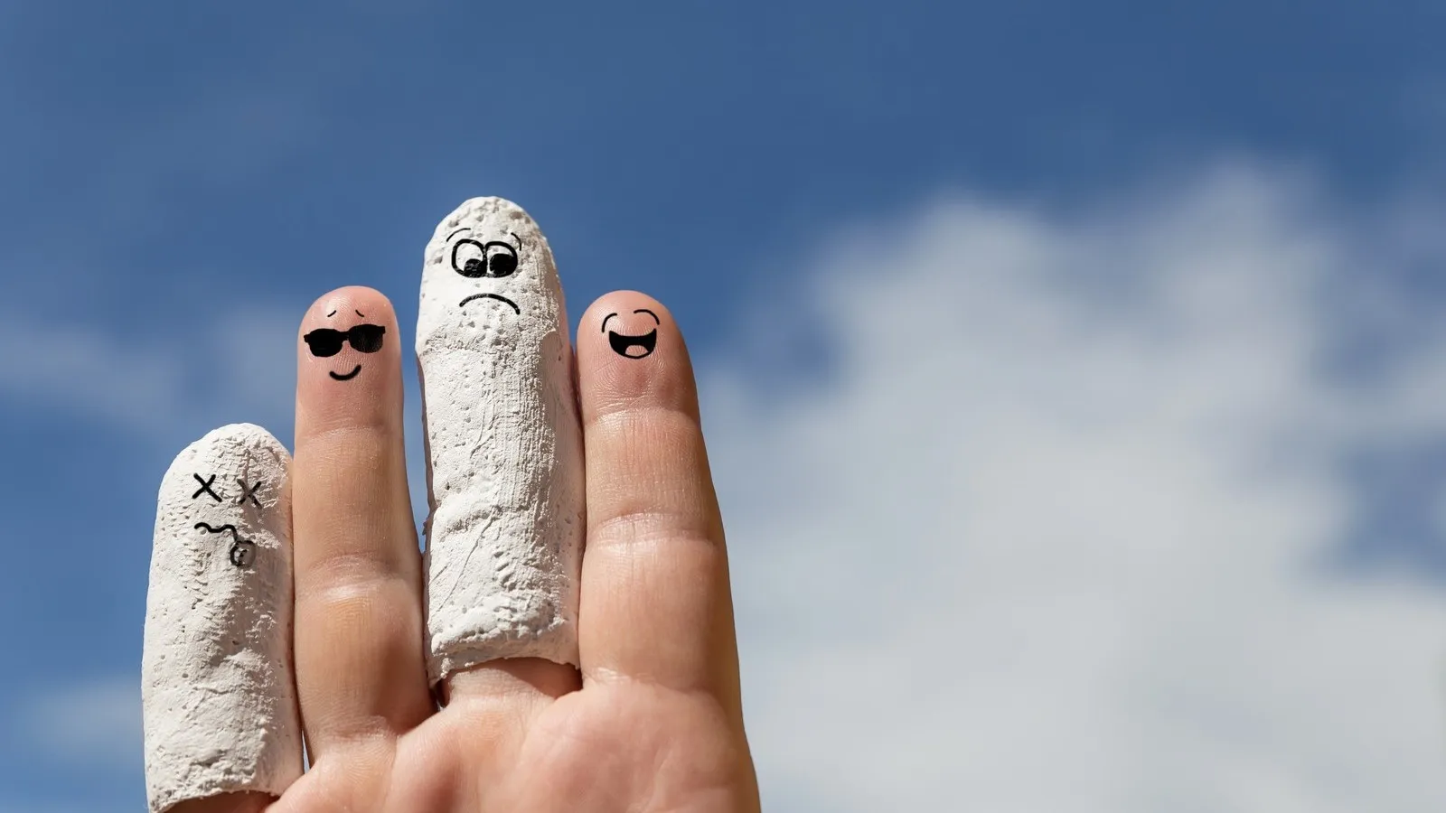 Hand vor blauem Himmel, eingegipste Finger mit Smiley bemalt.